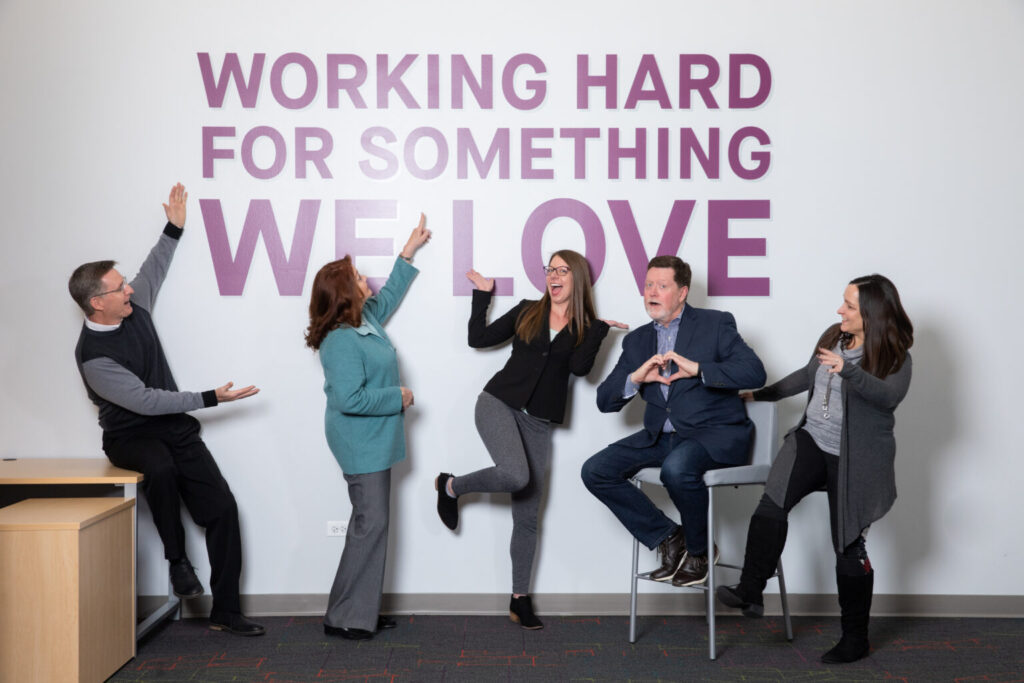 Group of business people in front of mural that says Working Hard For Something We Love